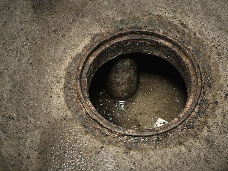 Open sewer cleanout in a concrete floor showing standing water in the lateral